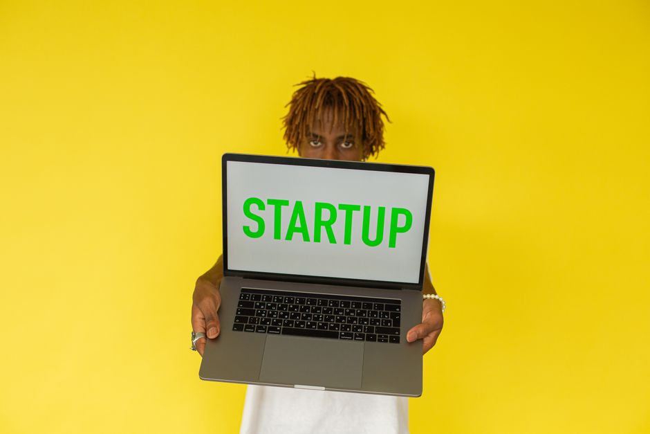 Joven emprendedor sosteniendo una laptop con la palabra Startup sobre fondo amarillo vibrante